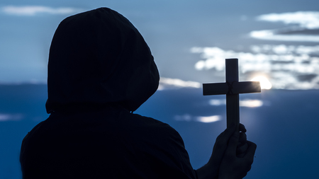 A man with a crucifix in his hands looks at the moon in the skyの写真素材