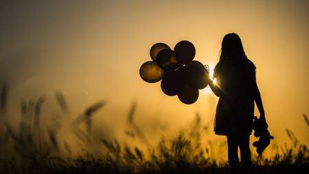 Silhouette of a girl with balloons and a teddy bear. It is worth the sunset. Farewell to childhood conceptの写真素材
