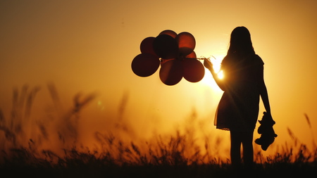 Silhouette of a girl with balloons and a teddy bear. It is worth the sunset. Farewell to childhood conceptの写真素材