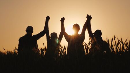 A group of successful young people hold hands, together they raise their upper hand. Successful team and team building concept.