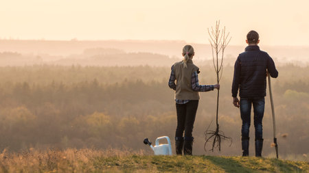 Young couple with a tree seedling and a shovel are standing nearby in a picturesque placeの写真素材