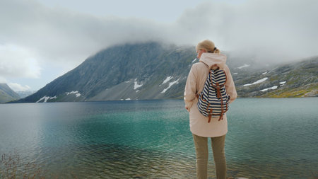 A woman admires a beautiful high mountain lake in the mountains of Norway.