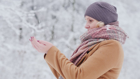 Attractive woman catches snowflakes in her palms, enjoys beautiful winter day