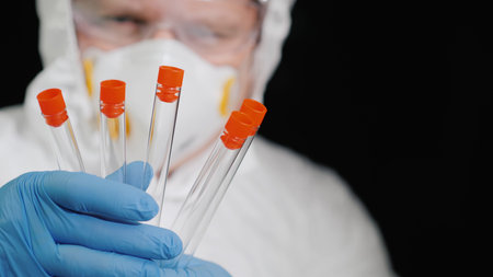 A researcher in a protective suit holds several test tubes