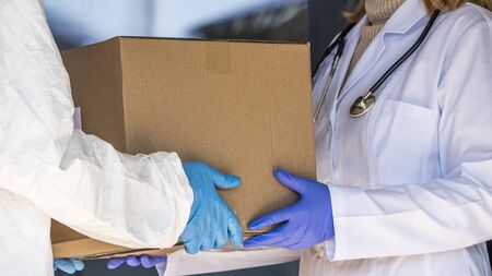 A person in a protective suit is handed a box of medicines to a doctor at the entrance to the hospitalの写真素材