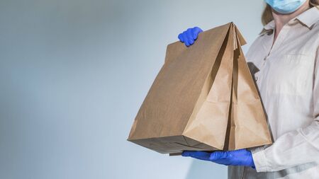 A man in protective gloves and a mask holds packets of food delivered to his homeの写真素材