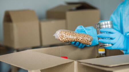 Man in protective suit packs grocery set into cardboard boxの写真素材