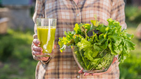 A woman holds a glass of green smoothie and a plate of lettuce. Healthy eating and diet