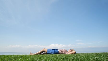 A woman is lying on the green grass, behind her you can see Lake Ontario.の写真素材