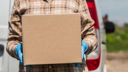 Courier with cardboard box in hand stands against the background of the delivery service vanの写真素材