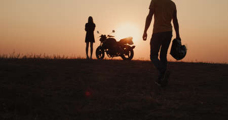 The silhouette of a man walking to the motorcycle where he is waiting for a young woman. Romantic travel conceptの写真素材