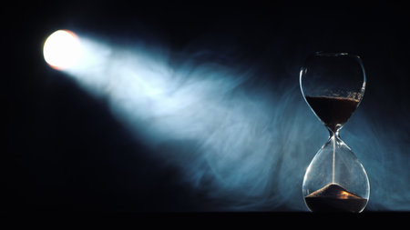Bright beam of the spotlight illuminates the hourglass, in the light of the swirling mistの写真素材