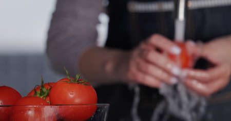 A bowl of tomatoes, in the background of a womans hand - washes tomatoes under a stream of water from a tapの写真素材