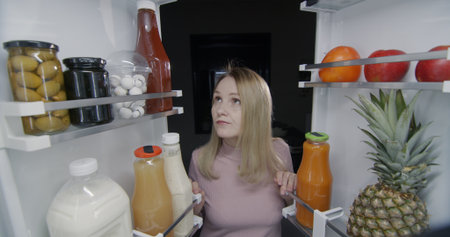 Portrait of a woman who looks into the refrigerator at night. Nighttime snacking and eating...
