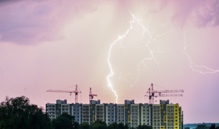 An apartment building with construction cranes against the background of the night sky where you can see lightningの写真素材