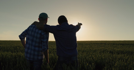 A man and his son watch the sunrise over a wheat field together. Farmers in the field and family businessの写真素材
