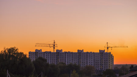 Sunset over the construction site of a multi-storey residential building. Cranes are visible in the...