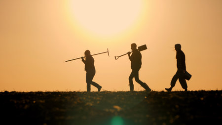 A family of farmers with working equipment walks through a field against the backdrop of a beautiful sunsetの写真素材