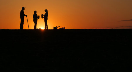 A group of farmers are preparing to plant seedlings in a field. Standing at sunsetの写真素材