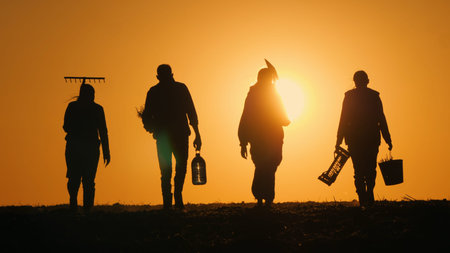 A family of farmers walks across a field towards the sunset. Carrying agricultural implements for...