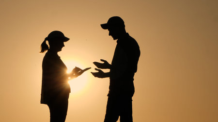 Silhouettes of two business people communicating outdoors, using a tablet