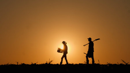Silhouettes of two farmers walking across a field with working equipment