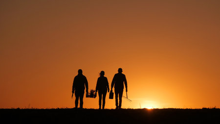Three farmers with equipment walk through a field at sunsetの写真素材