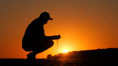 Silhouette of a farmer in a field holding a handful of earth in his handsの写真素材