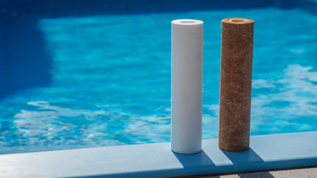 Two water filter cartridges, clean and dirty, standing by a swimming pool.の写真素材