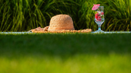 Straw hat and a glass with a refreshing drink by the pool, with green grass in the background