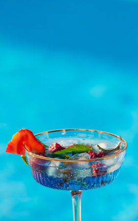 Refreshing blue cocktail with fruit garnish against a clear blue pool background