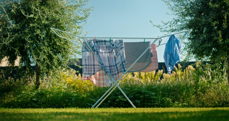 Clothes hanging on a laundry rack in a sunny backyard surrounded by lush greenery.
