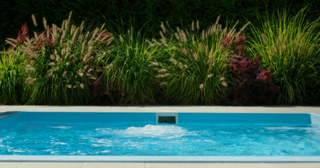 A clean swimming pool with bubbling water is set against a backdrop of lush, ornamental grasses.の写真素材