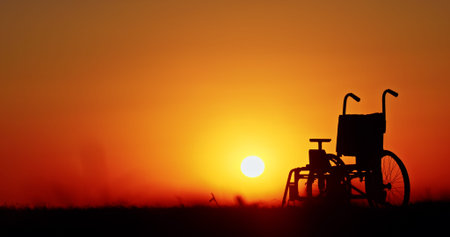 A wheelchair silhouetted against a vivid sunset, with a bright orange sky.