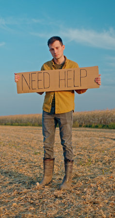 A young man stands in front of a cornfield, holding a sign that reads Need Helpの写真素材