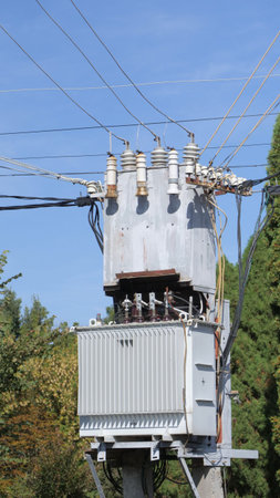 An electrical distribution transformer on a pole, connected to numerous wires, set against a natural backdrop.の写真素材