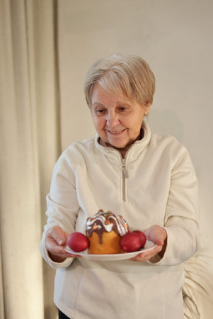 An elderly woman holding a plate with a decorated Easter cake topped with chocolate icing and...