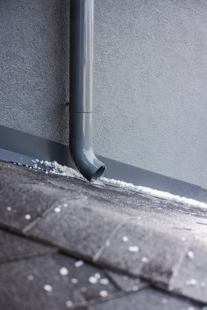 Close-up of water flowing from a gray downspout on a shingled roof covered with small hailstones.の写真素材
