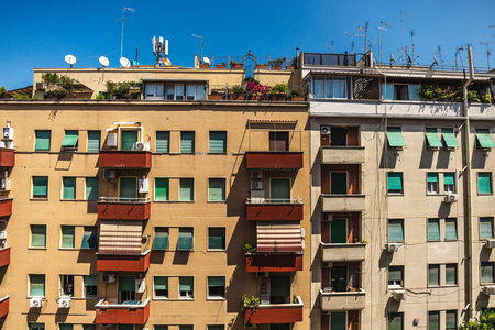 Facade of residential apartment buildings with balconies, plants and antennas under clear blue sky in Rome, Italyの写真素材