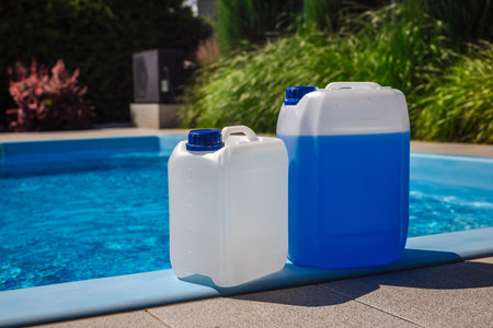White and blue plastic chemical canisters placed on the poolside edge next to a clean blue swimming...