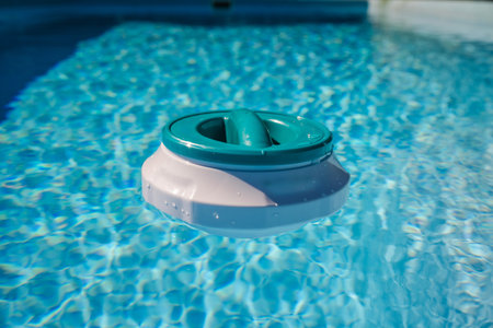Floating pool chlorinator on clear blue water surface, used for chemical disinfection and regular pool careの写真素材