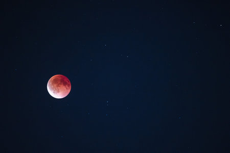 Blood moon during lunar eclipse glowing red in the night sky with visible stars aroundの写真素材