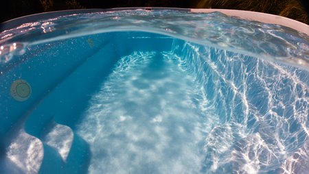 Sunlight dances on the steps and walls of a clear backyard pool, captured from an underwater perspective with surface ripples and refractions.の写真素材