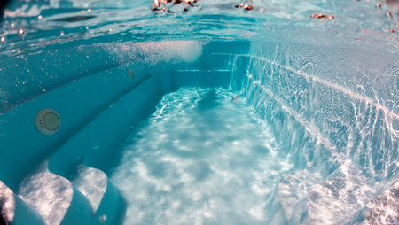 Underwater view of bubbling water and steps in a swimming pool, with bright reflections and clear blue tones creating a sense of motion and refreshment.の写真素材