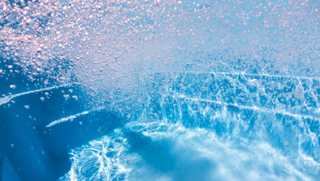 Underwater view of powerful bubbles and water turbulence in a clean pool, illuminated by sunlight with bright blue reflections.の写真素材
