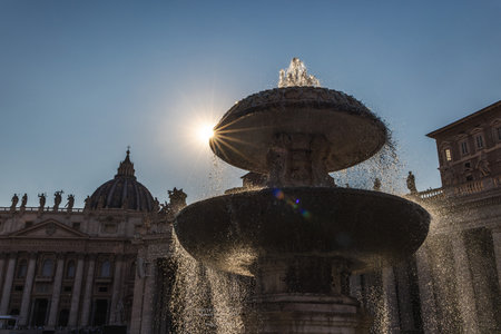 Fountain in St. Peters Square with the sun shining dramatically through water streams, Vatican City landmark at sunriseの写真素材