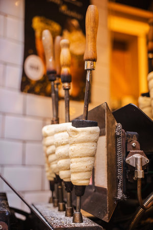 Traditional Czech chimney cakes called Trdelnik baking on rotating metal rods in a Prague street bakery, showing the preparation process of this famous sweet pastry.の写真素材