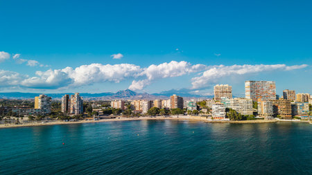 Aerial drone view of Alicante city coast in Spain with tall modern buildings, sandy beach, and calm Mediterranean sea on a bright summer dayの写真素材