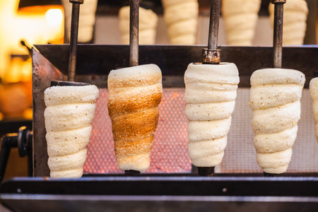 Traditional Czech trdelnik pastries roasting over an open flame on metal rods in a bakery in Prague,...
