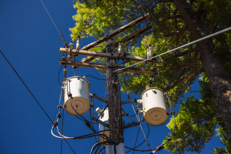 Wooden utility pole with power transformers and electrical cables against blue sky in the United...
